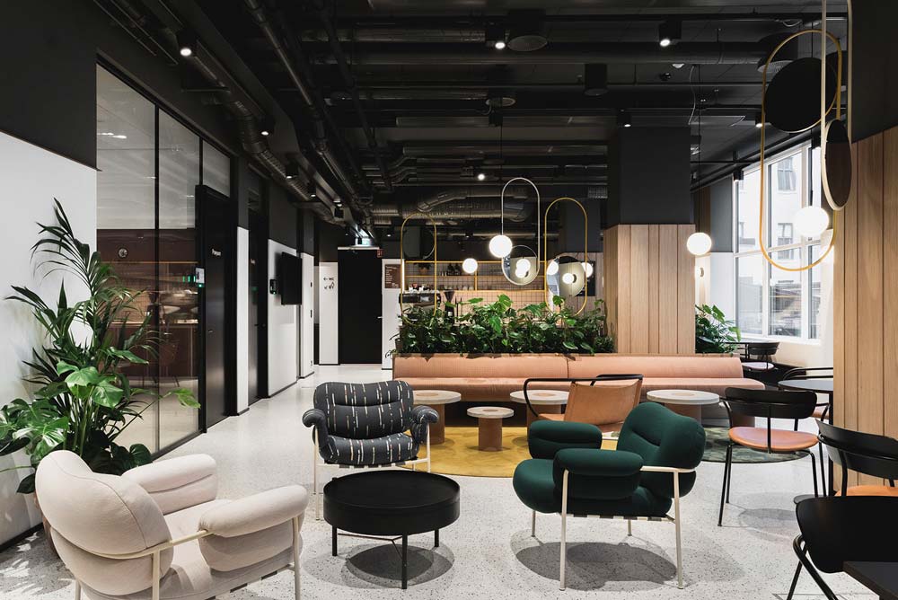 Une cafétéria d'entreprise confortable avec des fauteuils, des banquettes, de la verdure et une grande baie vitrée