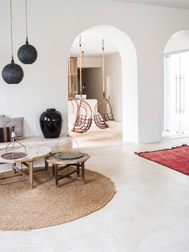 Un salon blanc avec un tapis rond et deux fauteuils suspendus en bois