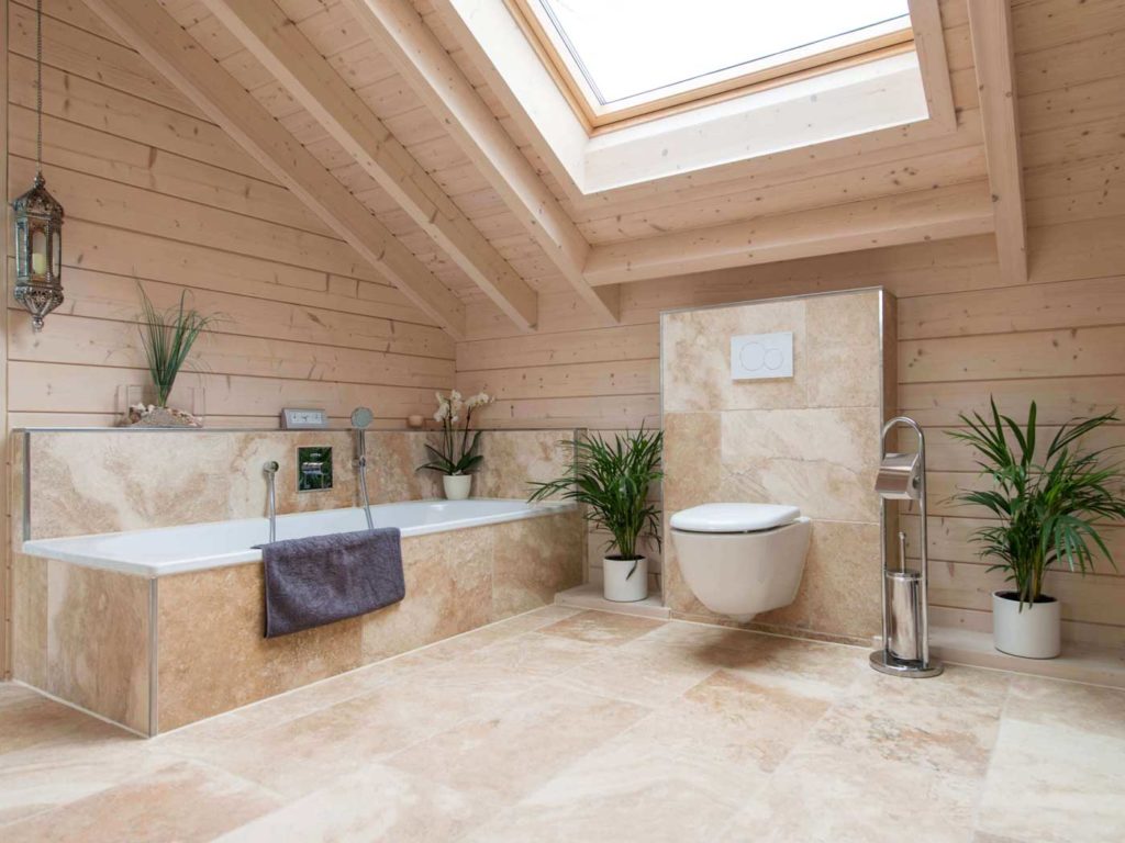 Une salle de bain en travertin sablé et en bois blond avec une baignoire et un velux lumineux