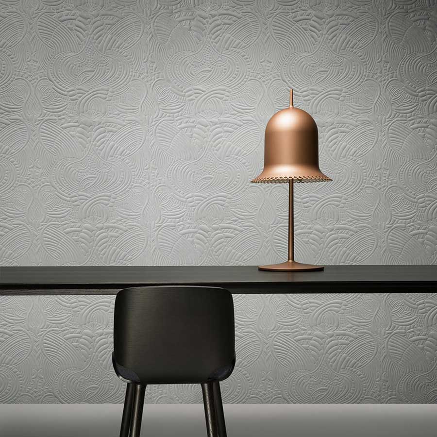 Du mobilier de bureau noir devant un mur textile blanc avec une lampe de bureau rose gold