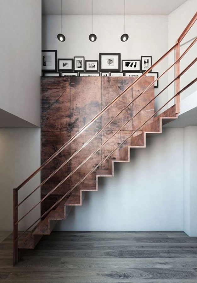 Un escalier tout en cuivre oxydé dans un intérieur minimaliste où les murs sont blancs et où il y a de la petite décoration comprenant des lustres noirs et des photographies en noir et blanc