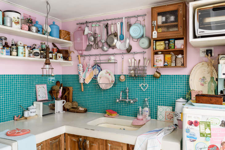 Une cuisine kitsch avec une mosaïque bleu azur et rose bonbon. Les ustensiles trônent fièrement au dessus des plans de travail et offrent un spectacle visuel.
