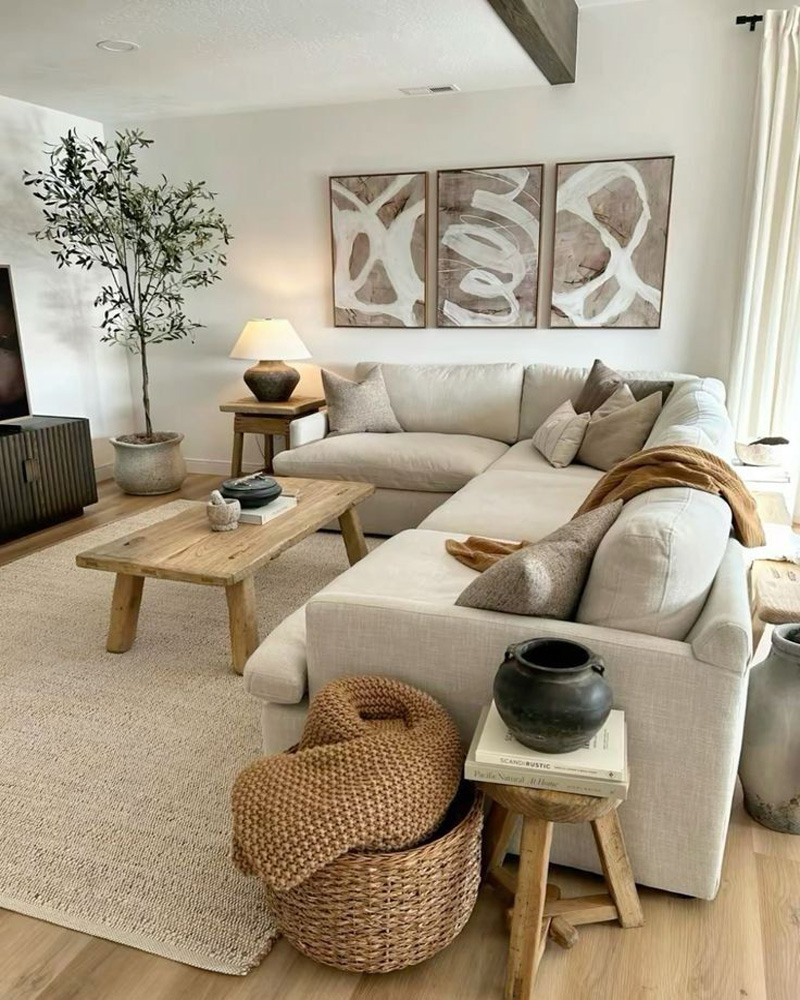 Salon avec tapis tissé, un canapé couleur galet, un tableau avec des motif de couleurs marron et gris. Des rangements avec des sacs en osier.