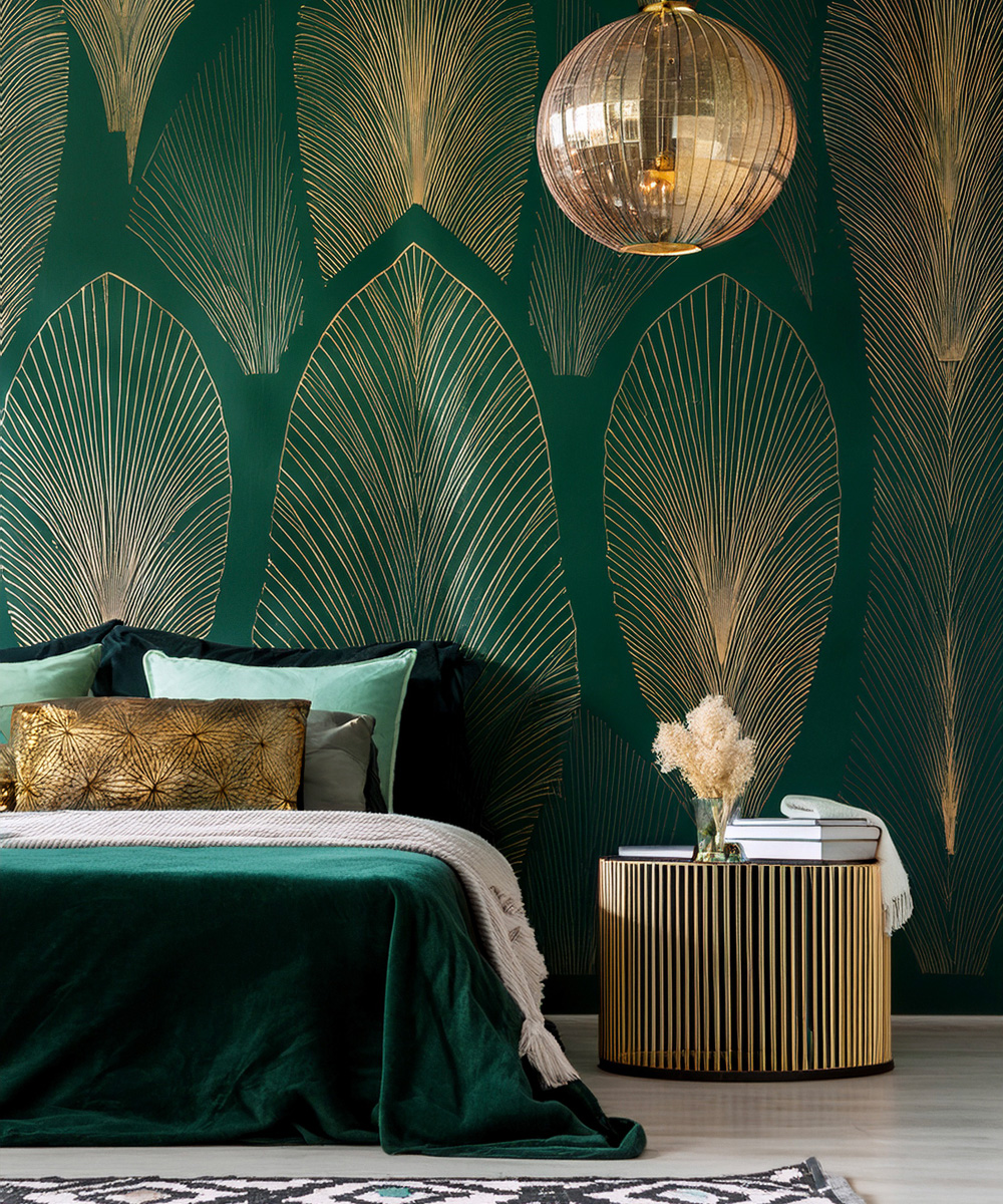 Chambre chic, avec un vert très profond, avec de grandes feuilles de couleurs dorées en tapisserie, accompagné d'autres éléments dorés, comme la table de chevet et la tête de lampe.