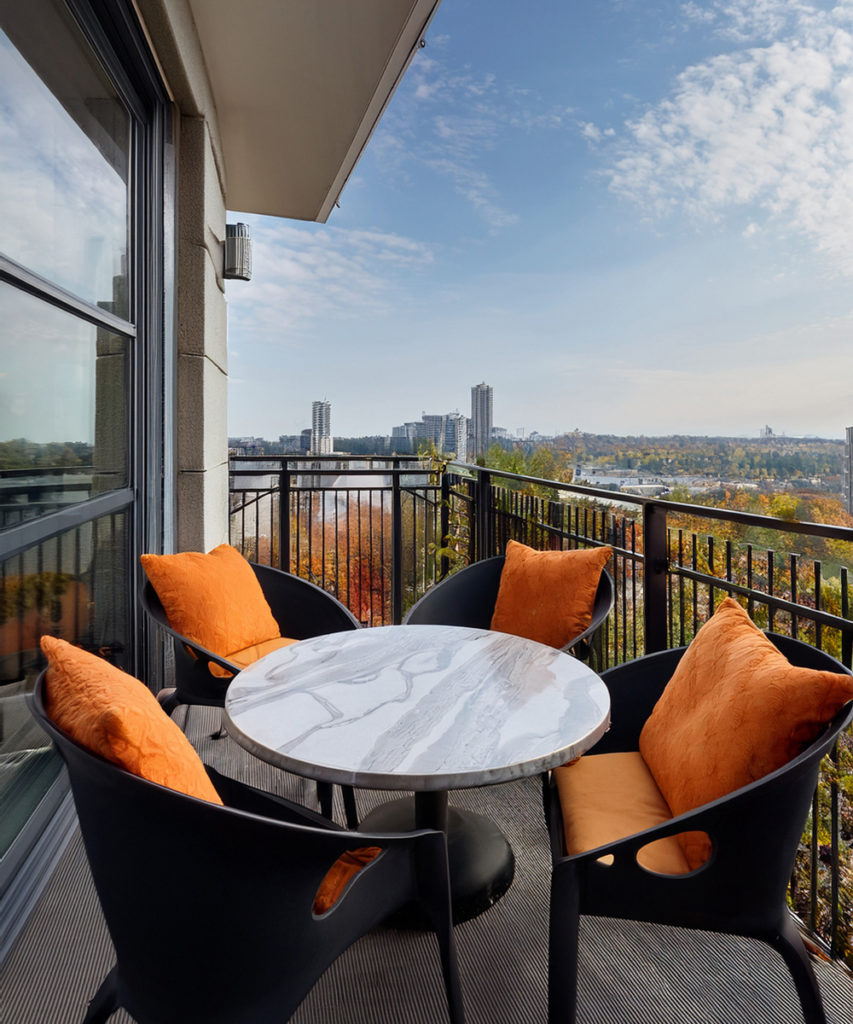 Salon de jardin sur un balcon, avec des assises noire, et des coussins orange automne et une petite table ronde imitation marbre.