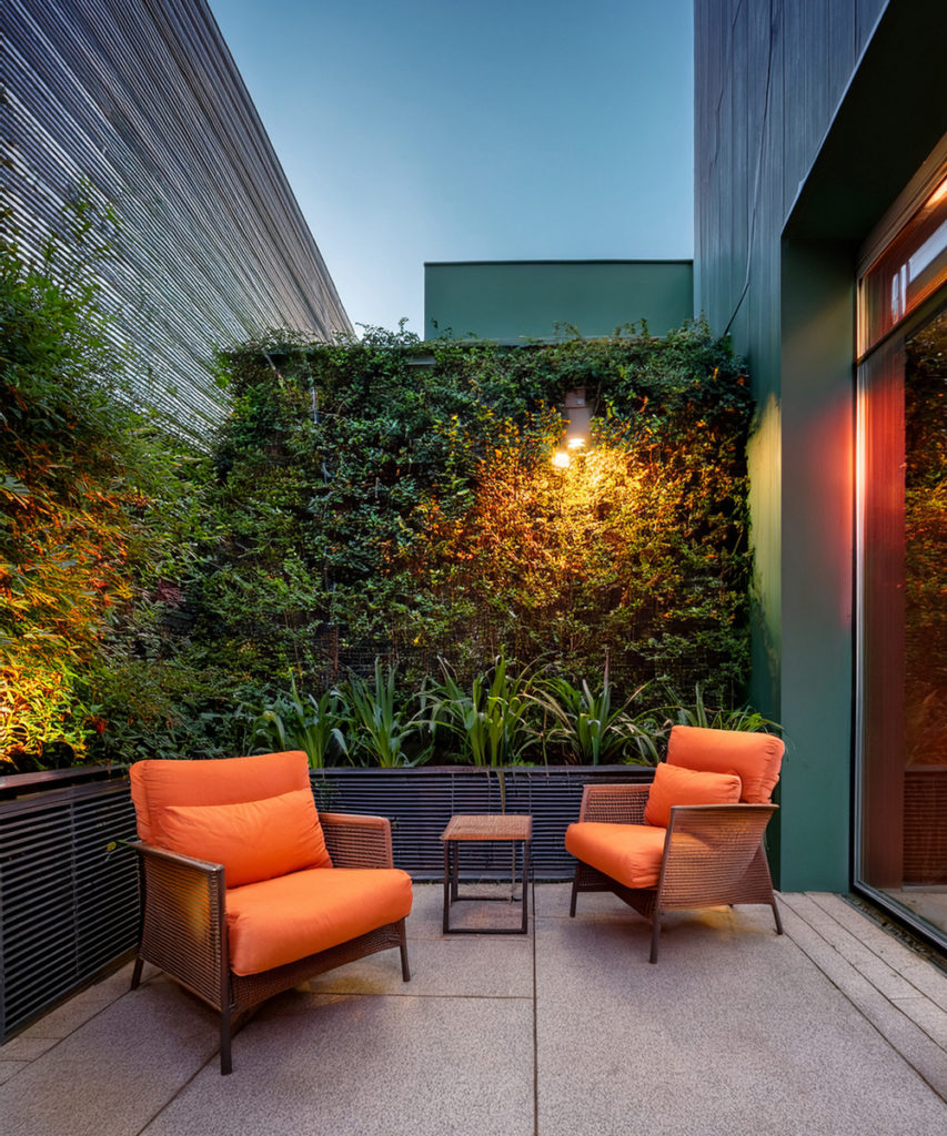 Salon de terrasse avec une petite table basse en bois carré, et deux gros fauteuils en acier noir avec des coussins orange.
