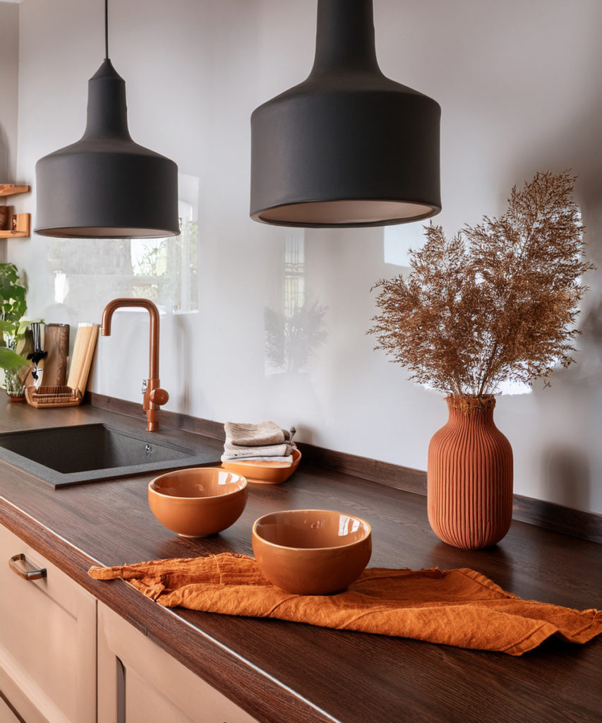Plan de travail de cuisine en bois foncé, avec des luminaires noir mat, et des accessoires de cuisine couleur terracotta et orange.