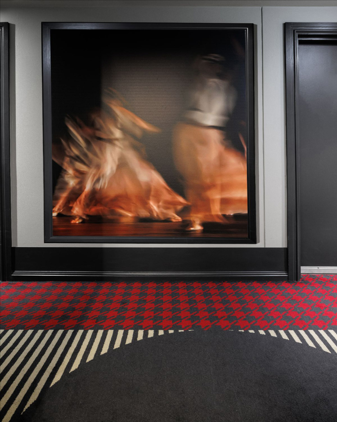 Hall d'accueil d'un hôtel avec un tapis avec des formes pied-de-poule et l'autre en rayure noir et blanche.